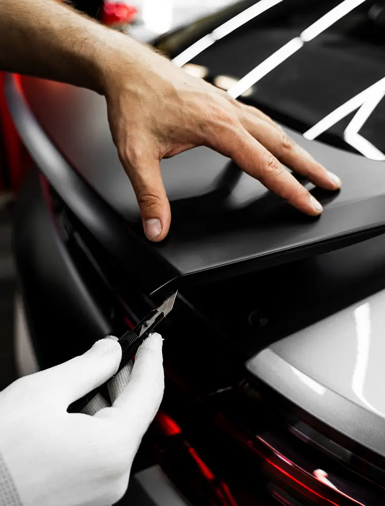 Technician trimming black vinyl wrap during professional vehicle wrap installation