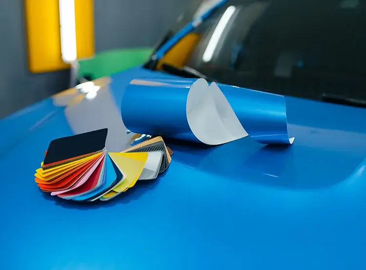 Vinyl car wrap color and finish samples displayed on a blue wrapped vehicle