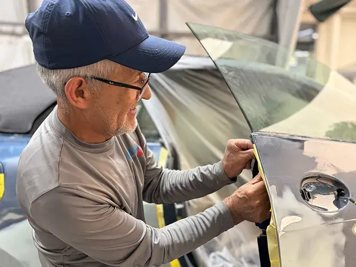 Collision repair technician repairing a vehicle door at Fireplace Auto Collision in East Hampton, NY.