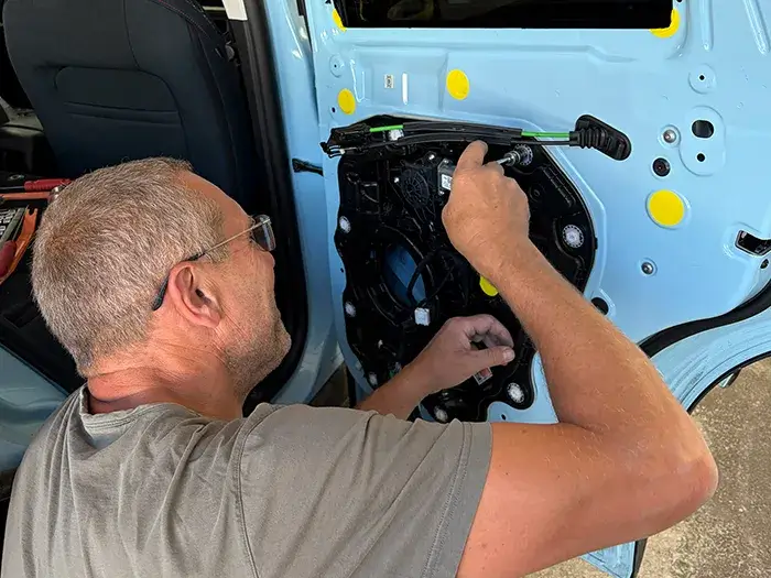 Collision repair technician installing door components during vehicle reassembly at Fireplace Auto Collision.